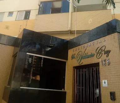 Detalhe da entrada: o nome Residencial Dr. Valdemiro Cruz em letras cursivas de metal sobre parede de pastilhas amarelas, com o número 185, ao lado do bloco de granito preto da portaria.
